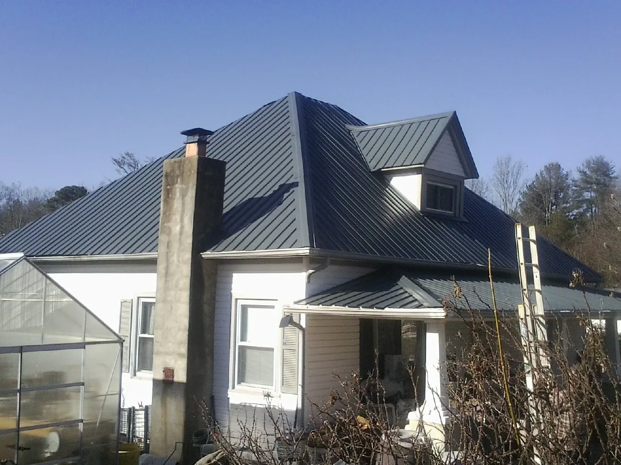 Dark blue standing seam metal roof on a white farmhouse with dormer — Slate & Tile Roof Repair by Roofing Brothers in Bonita Springs