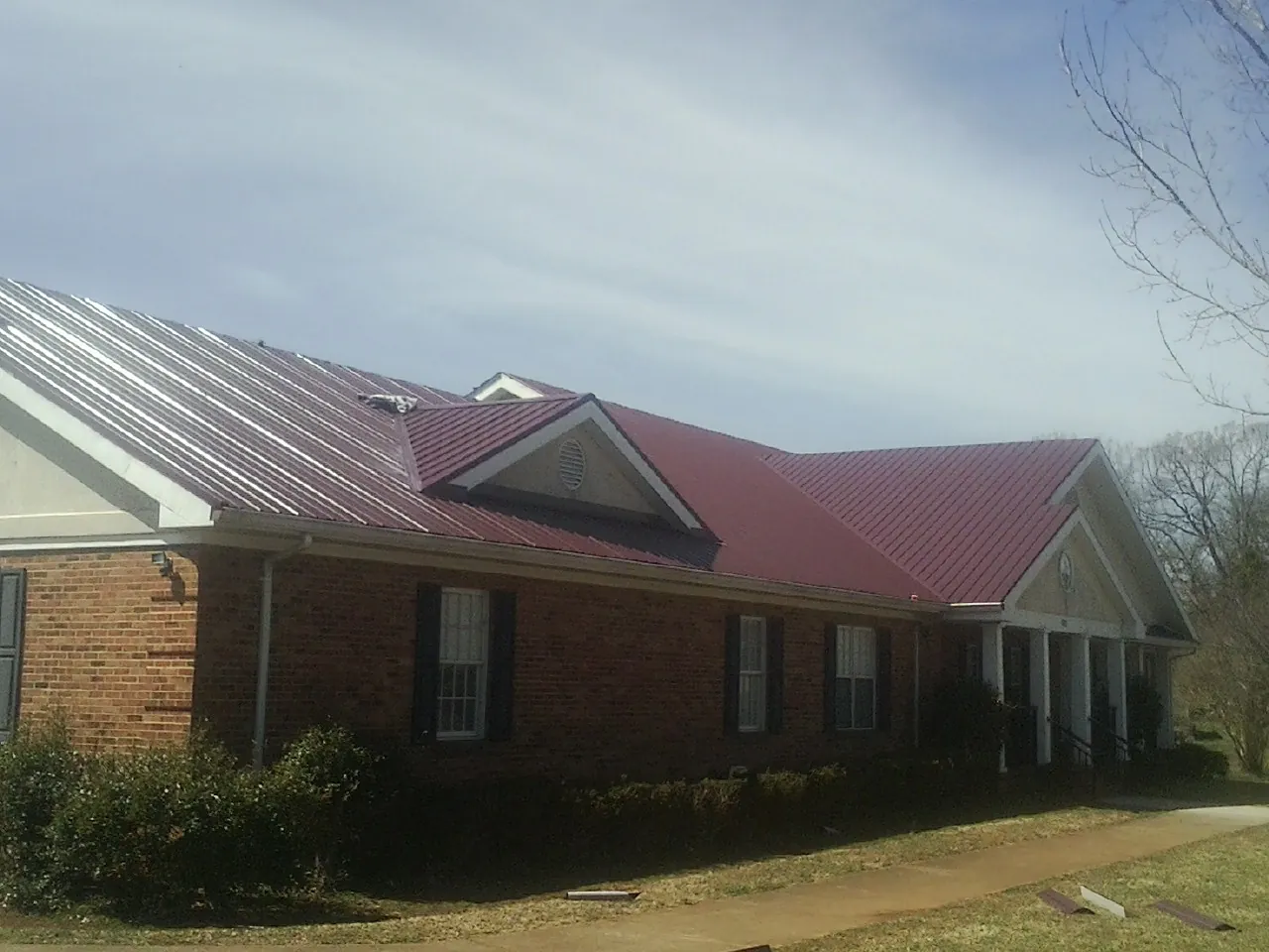 Red metal roof with gabled entries on a long brick building, from a Hail Damage Roof Repair job in Bonita Springs