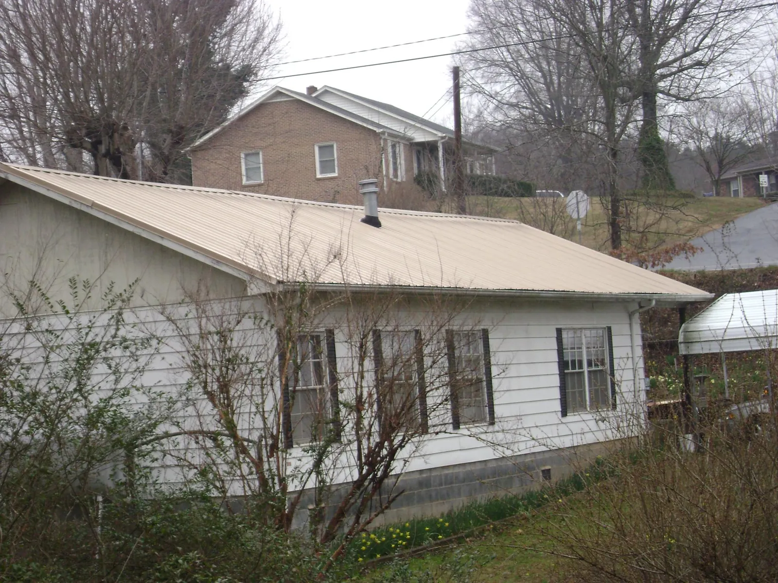 Tan metal roof on a white sided house set into a hillside — Commercial Roofing by Roofing Brothers in Bonita Springs